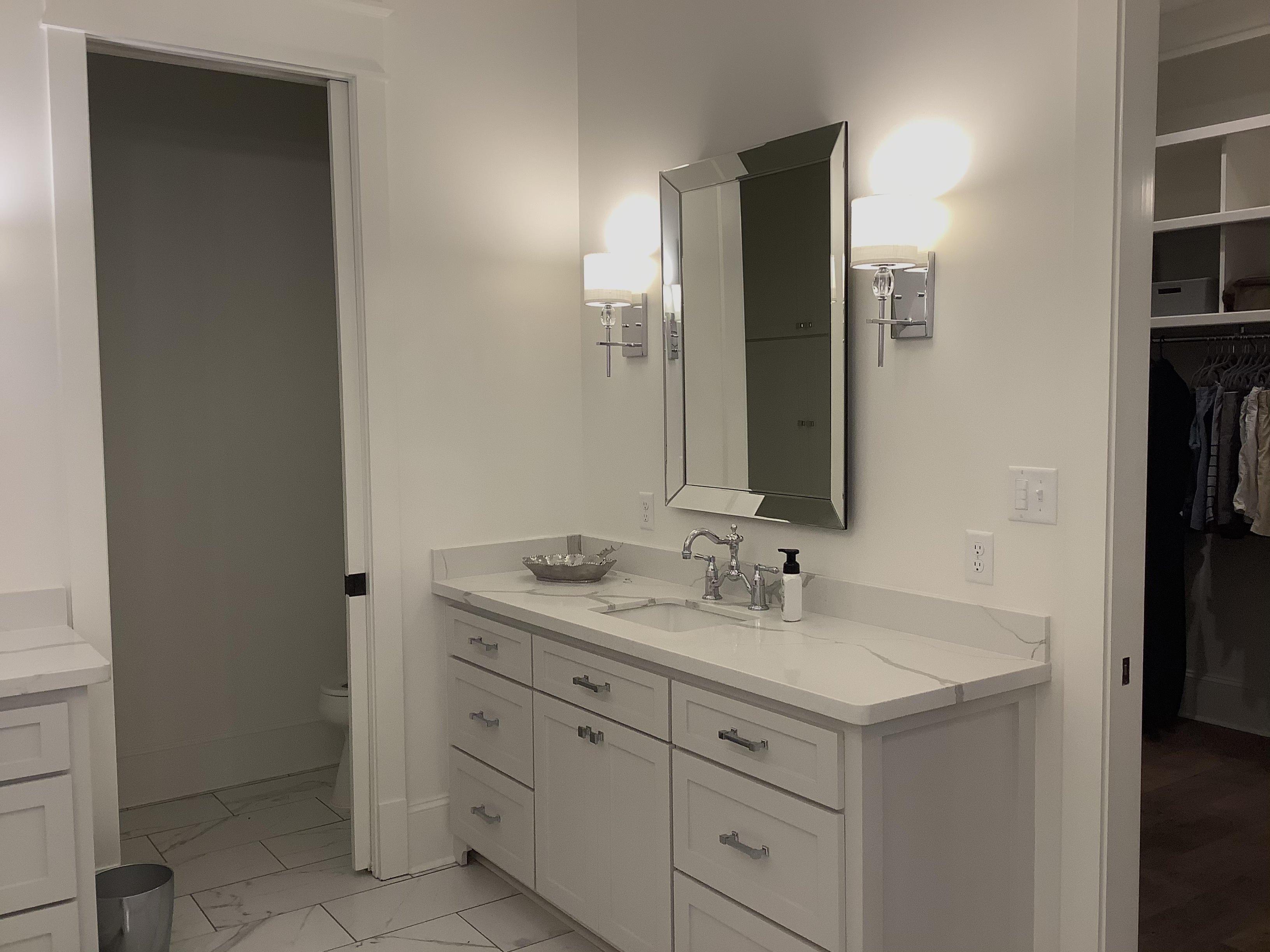 White bathroom with marble counter and wall sconces